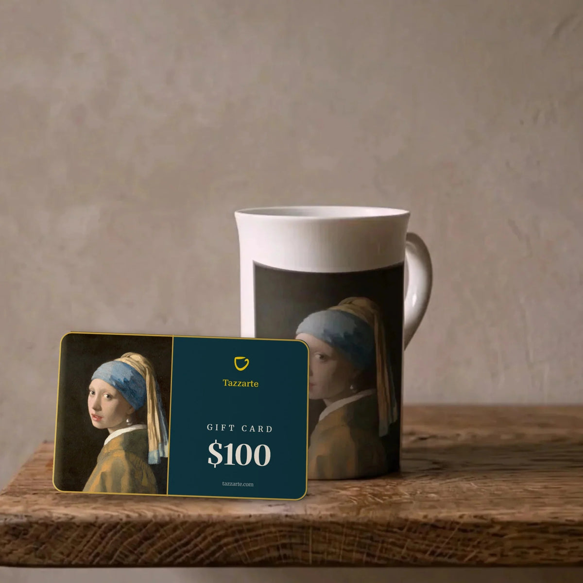 Tazzarte-Kunstgeschenkkarte über $100 mit Vermeers Mädchen mit dem Perlenohrring neben der passenden Kunsttasse aus Porzellan auf einem Eichenregal