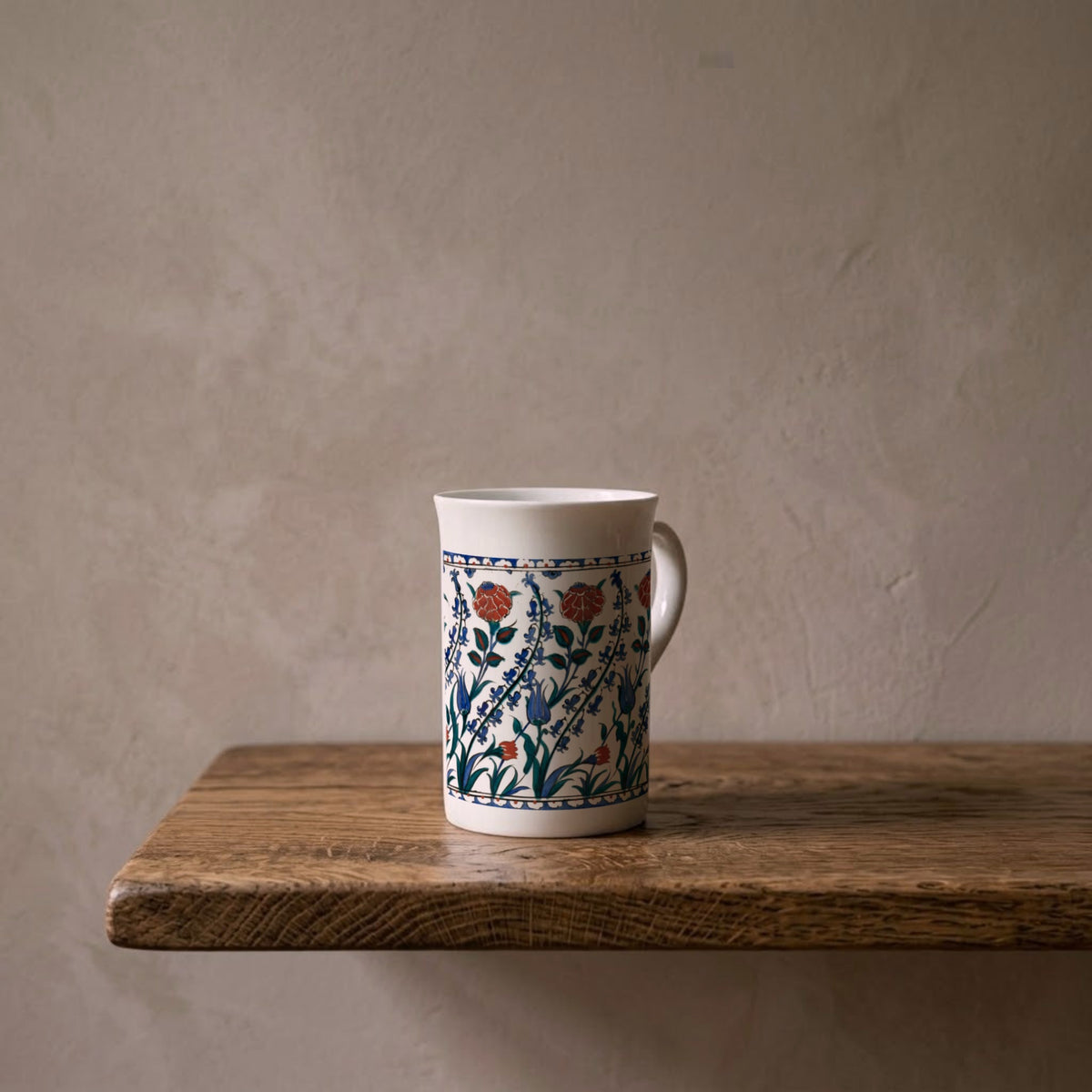 Iznik tankard with tulips and carnations – porcelain art mug on an oiled oak shelf against a limewashed wall